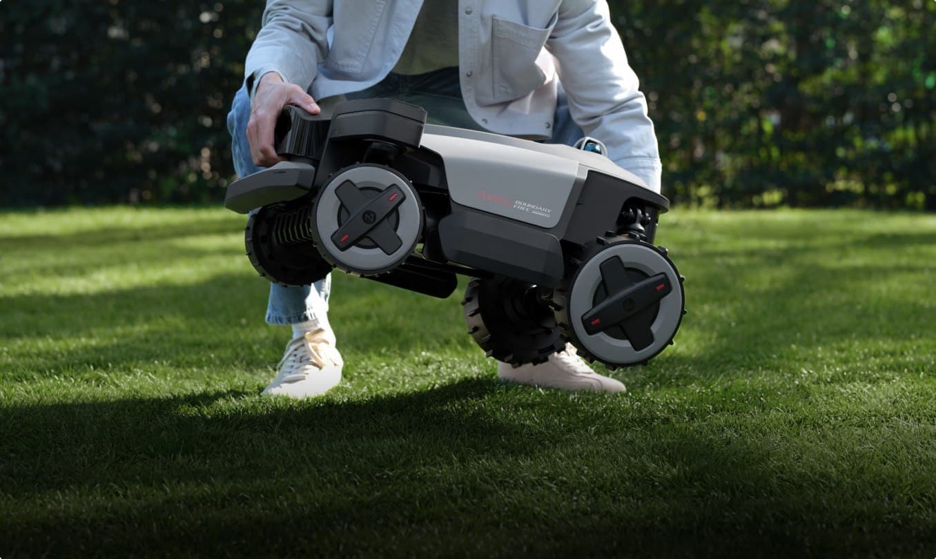 Uporabnik dviguje robotsko kosilnico Roborock RockMow na vrtni trati